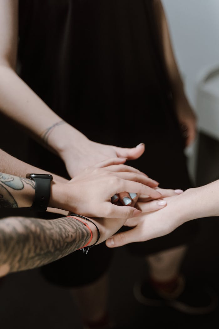 Close-up of diverse hands with tattoos joining together in a team huddle.